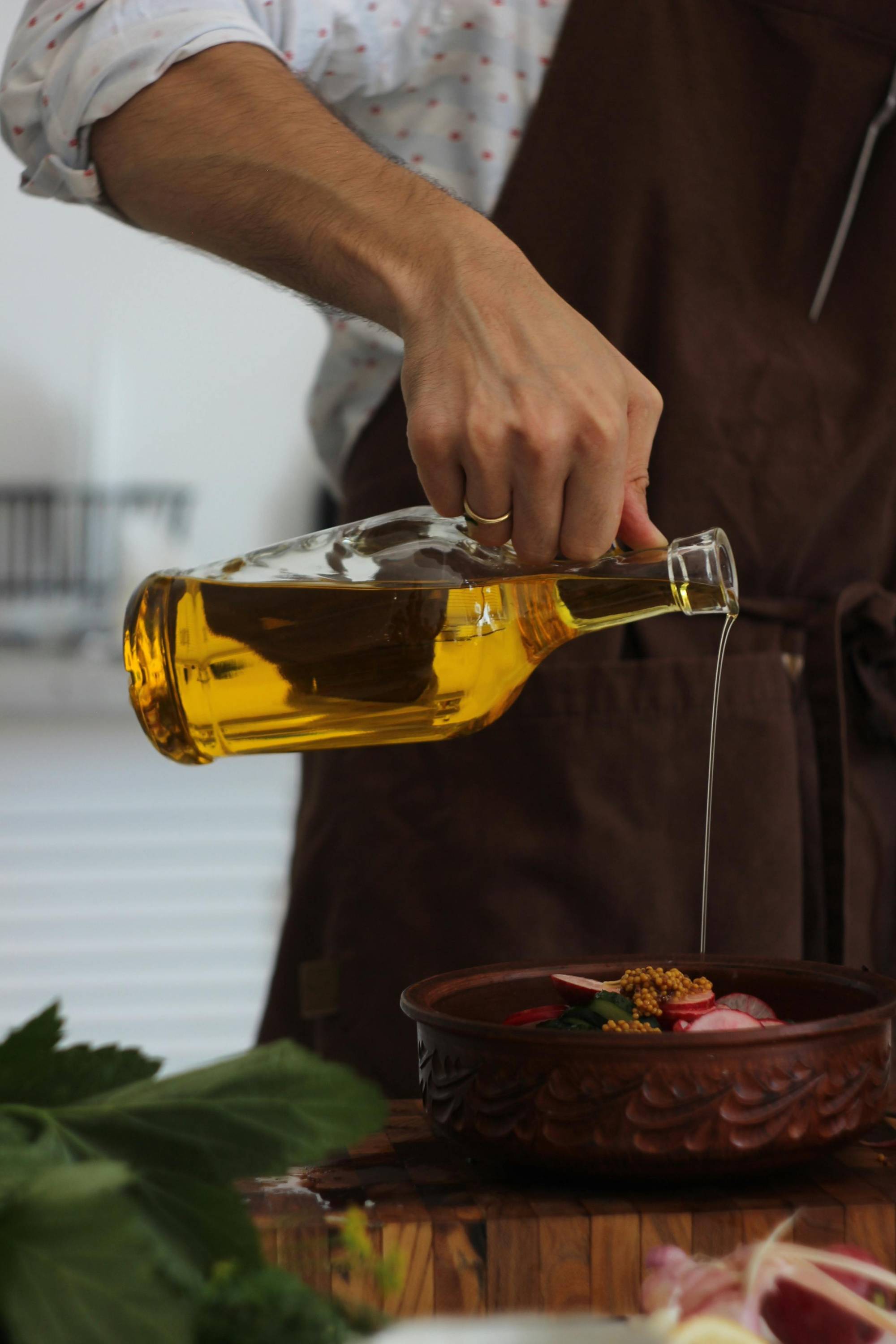 Hand pouring clear glass bottle of olive oil into food dish
